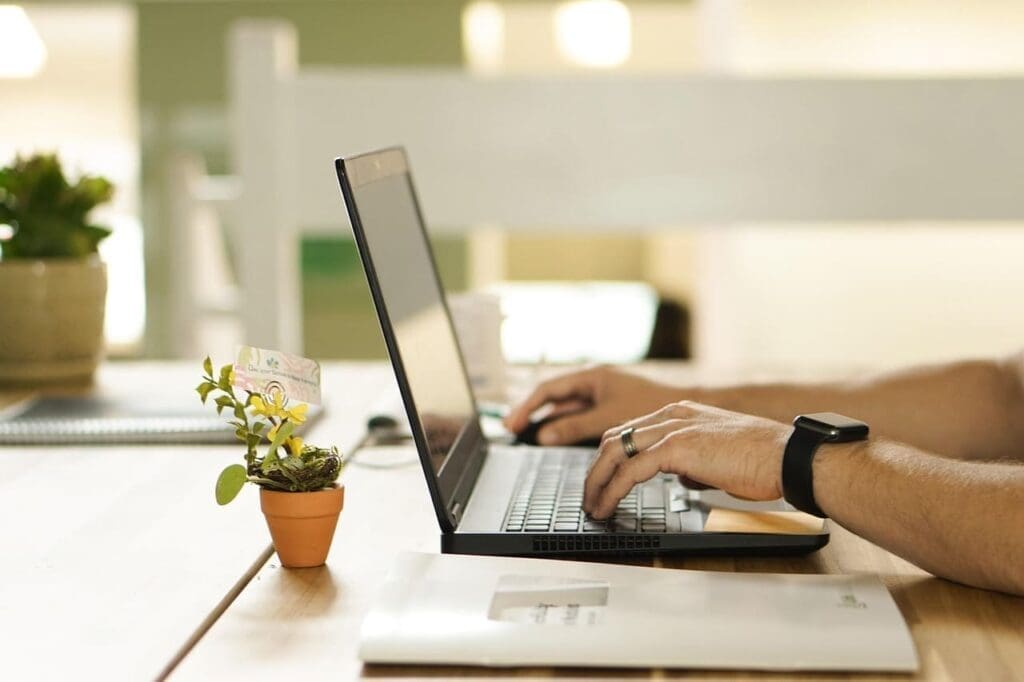 Ujęcie boczne przedstawiające laptopa na biurku i pracujące na nim dłonie